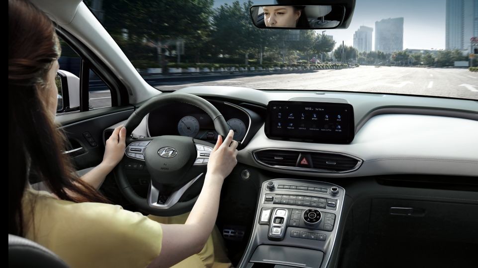 Pohled na řidičku za volantem nového sedmimístného SUV Hyundai SANTA FE Hybrid jedoucího ve městě.